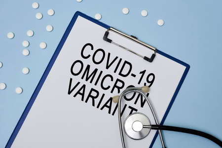 A clipboard with Covid Omicron variant text and stethoscope. Medical background made of pasteboard, stethoscope and drugs or white pills on color background. Covid-19 omicron variantの写真素材