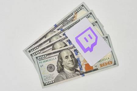 Tashkent, Uzbekistan - 22 November, 2021: Pile of us dollars and Twitch logo. Twitch logo on card...