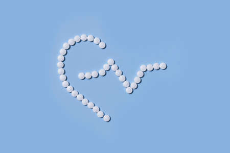 Group of white round pills forms heart figure next to heart rhythms from white pills on a blue background. Theme of health care, medical treatment and disease prevention.の写真素材