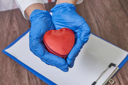 Doctor hands holding heart, donation and implantation, medic saving life on notebook. Notebook for recording the results of a patient examination.の写真素材