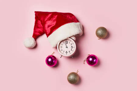 Christmas time consept.Christmas clock in a Santa Claus hat or cap on a pink background. The minute hand at twelve oclock on New Years Eve.の写真素材