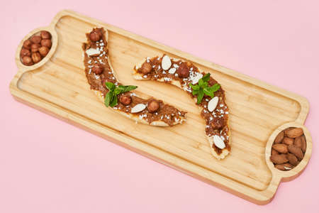 Bananas with peanut butter, almonds and nuts, on wood plate on wooden plate. Healthy food. Close upの写真素材