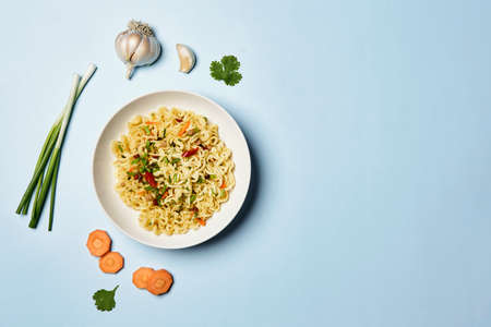 Instant noodles composition. Noodles and fresh vegetables and spices on bright blue backgroundの写真素材