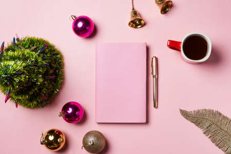 Home office table with Christmas decorations, coffee cup and notebook on pink backgraund. Flat lay, top view. Christmas workspace.の写真素材