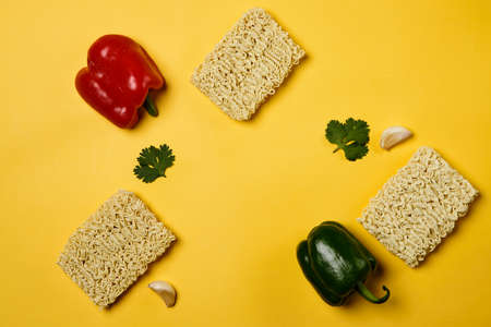 Instant noodles composition. Noodles and fresh vegetables and spices on yellow backgroundの写真素材