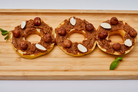 Apple rounds dialed on top of each other with peanut butter, almonds and nuts, on wood plateの写真素材