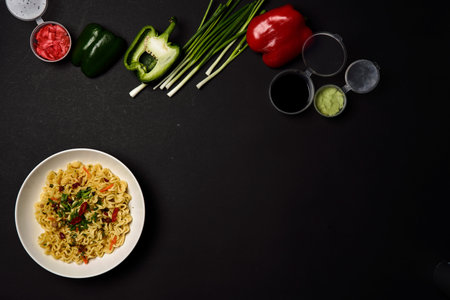 Instant noodles composition. Noodles and fresh vegetables and spices on bright black background