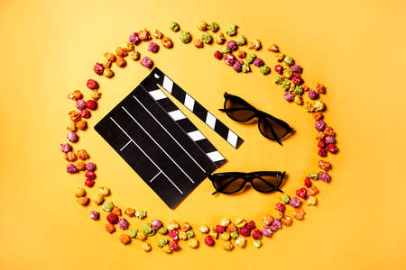 Movie clapper, pop corn and 3d glasses in a yellow background. Flat lay. Cinema party concept.の写真素材