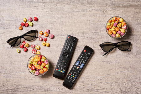 Popcorn, 3D glasses and TV remote on wooden background. Concept of watching movies at home. View from aboveの写真素材