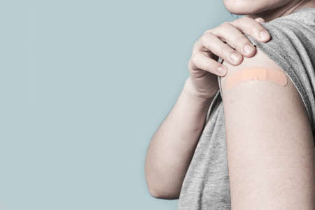 Woman after getting a vaccine. Female holding her silver shirt sleeve and showing her arm with bandage after receiving vaccination. Concept of recommended inoculationの写真素材