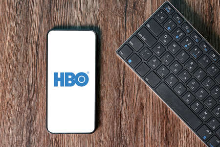 Miami, USA - 03.26.2021: HBO Max app on the smartphone screen on wooden background with a computer beside it. App for movies and TV series via streamingのeditorial素材