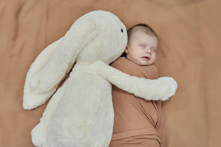 Newborn baby with her white bunny toy. Cute mixed race baby girl sleeping in the bedの写真素材