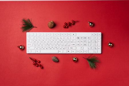 a computer keyboard on a red surface with christmas decorations around it and pine cones in the top right hand cornerの写真素材