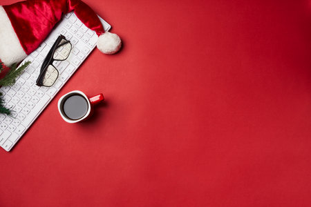 an office desk with a computer, keyboard and christmas hat on its red surface next to a cup of coffeeの写真素材