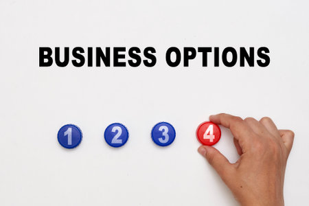 a persons hand writing the word business on a white surface with three red and one blue buttons in different sizesの写真素材
