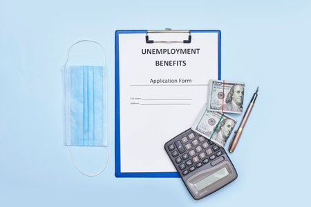 a notepad, pen, calcula and money on a clipboard with the words unemployment benefits written on itの写真素材