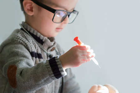 a young boy with glasses holding a tooth and looking at the camera while he is putting something in his handの写真素材