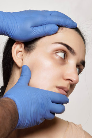 a womans face and hands with blue gloves on, as she is getting her botilage treatmentの写真素材