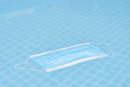 a face mask floating in a swimming pool, with water droplets on the surface to protect from...