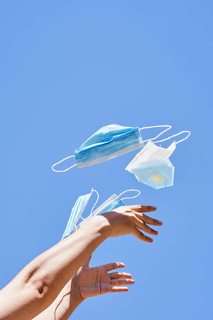 someones hand holding up a pair of surgical masks in the air against a blue sky with no cloudsの写真素材