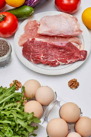some meat, eggs and vegetables on a white table with an egg in the middle next to it is a knifeの写真素材