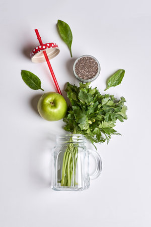 an apple, parise, and some greens on a white surface with a red straw in the photo is taken from aboveの写真素材