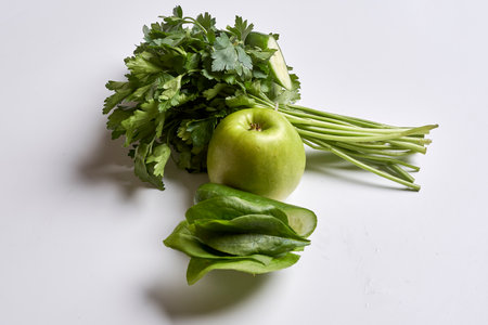 some green vegetables on a white surface, including an apple and ceince leaves with parise in the backgroundの写真素材