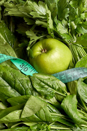 some green vegetables and an apple with a measuring tape around it to measure the size of their leafy leavesの写真素材