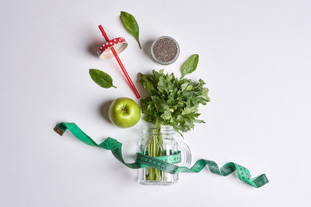 an apple and some green leaves in a glass jar with a measuring tape around it, on a white backgroundの写真素材