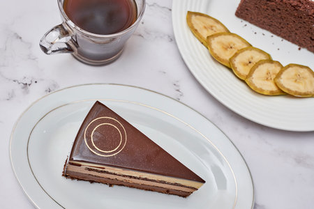a piece of chocolate cake on a plate with a cup of coffee and banana slices in the photo is takenの写真素材