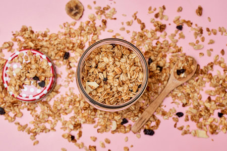 granos in a glass jar on a pink background with spoons full of granos and oats scattered around itの写真素材