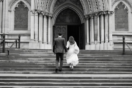 a bride and groom walking up the stairs in front of an old building on their wedding day black and whiteの素材