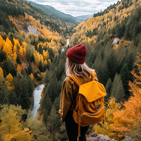 a woman with a backpack looking out over the mountains and trees in autumn, wearing a red beanie hatの素材