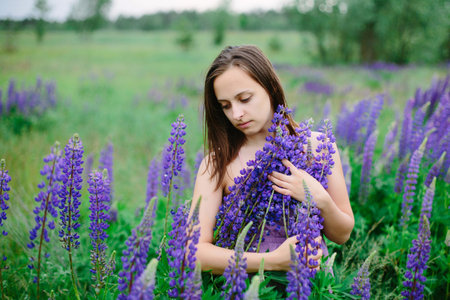 Beautiful young girl in ultra violet dress holding a bouquet of lupine at sunset on the field. The concept of nature and romance.の写真素材