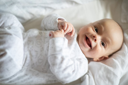 Adorable baby boy in white bedroom. Newborn child relaxing in bed. Nursery for young children. Textile and bedding for kids. Family morning at home. lifestyle concept, real life.の写真素材