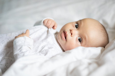 Adorable baby boy in white bedroom. Newborn child relaxing in bed. Nursery for young children. Textile and bedding for kids. Family morning at home. lifestyle concept, real life.の写真素材