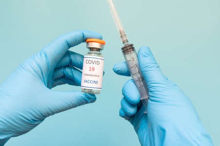 Coronavirus Vaccine in glass bottle in hand of doctor blue vaccine jar on white background. Vaccine Conceptの写真素材