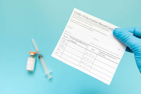 Doctor is holding a vaccination record card and corona virus vaccine vials. Passport of immunity to the coronavirus in the hands of a male doctor. Health passport.の写真素材