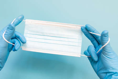 Doctor hand wear blue medical gloves holds antivirus face mask on blue background for pandemic, airborne diseases, outbreak, concept. Copy spece.の写真素材