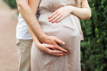 Man Hands Hug Pregnant Woman by Belly Closeup Photography. Staying Beautiful Pregnancy Girl Dressed in Dress. Future Parents and Childbirth Horizontalの写真素材