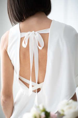 Brunette woman standing in front of a white wall with her back to the camera. Dress with a beautiful back.の写真素材