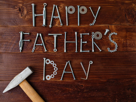 Text Happy Fathers day made from metallic bolts and iron nails with hammer on wooden background....