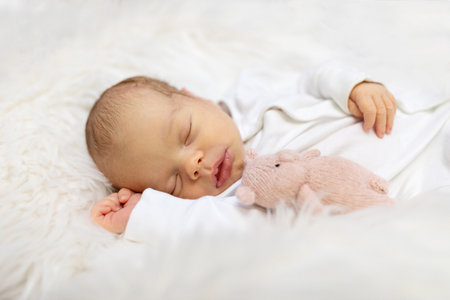 Adorable newborn one week age in white bedroom. Newborn child relaxing in bed. Nursery for young children. Textile and bedding for kids. Family morning at home. Lifestyle concept, real life.の写真素材