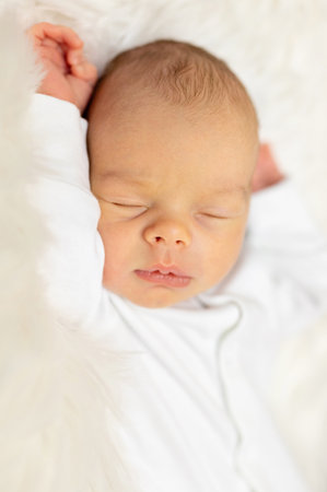 Adorable newborn one week age in white bedroom. Newborn child relaxing in bed. Nursery for young children. Textile and bedding for kids. Family morning at home. Lifestyle concept, real life.の写真素材