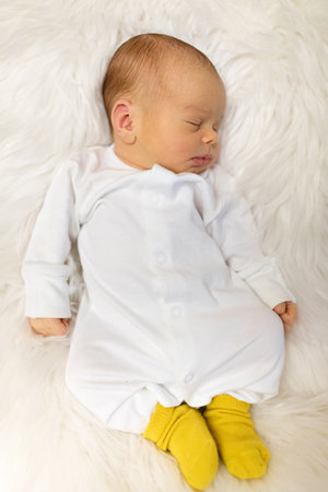 Adorable newborn one week age in white bedroom. Newborn child relaxing in bed. Nursery for young children. Textile and bedding for kids. Family morning at home. Lifestyle concept, real life.の写真素材