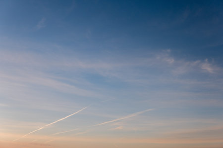 A blue sky pattern with a small amount of clouds with traces of aircraft
