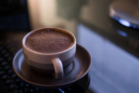 a cup of coffee with delicious foam in the light from the monitor in the eveningの写真素材