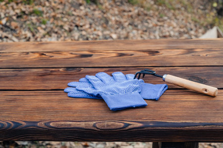 folded blue fabric gloves with a dotted coating and a small black cultivator rake with a wooden...