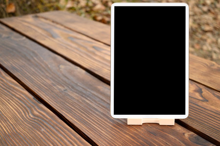 white tablet with a clean black screen stands on a small light stand, set on a brown wooden table, leaving plenty of space for text or graphics on the sideの写真素材