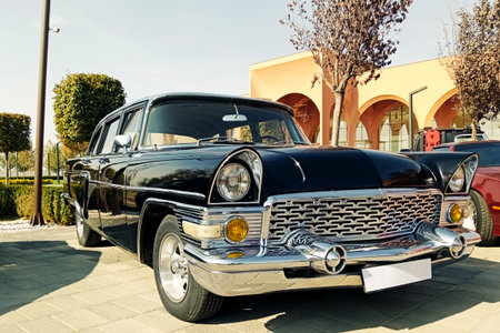 a close-up, low-angle shot of a luxurious black vintage automobile featuring polished chrome trim and a large radiator grille, displayed outdoors on a clear, sunny afternoonの写真素材